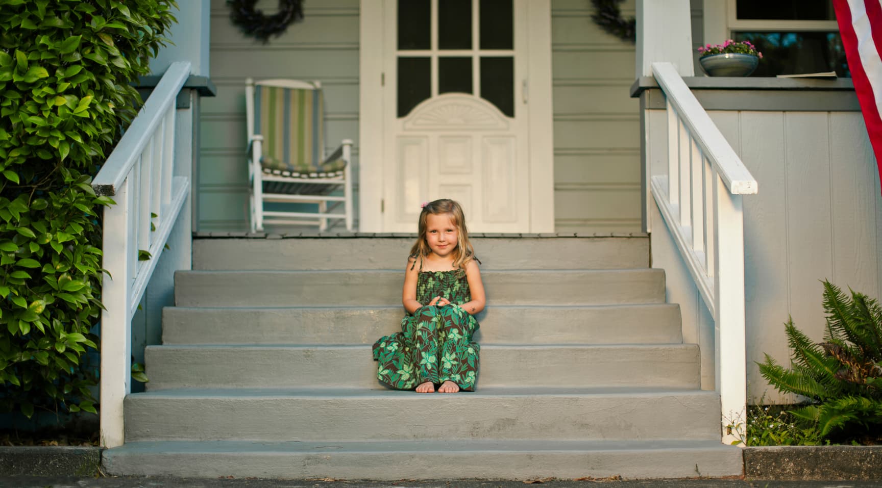 Young child sits on steps of weatherboard house